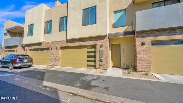 townhome / multi-family property with a garage, stucco siding, and brick siding