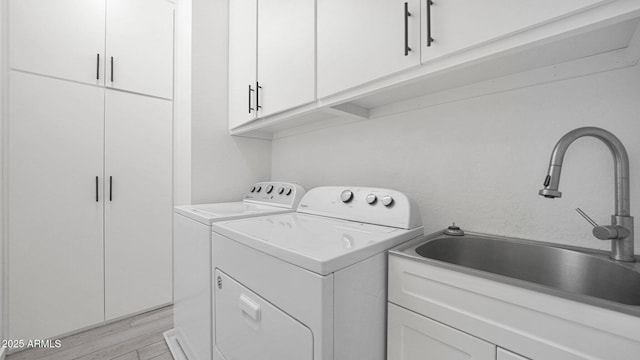 laundry room featuring separate washer and dryer, light wood-type flooring, a sink, and cabinet space