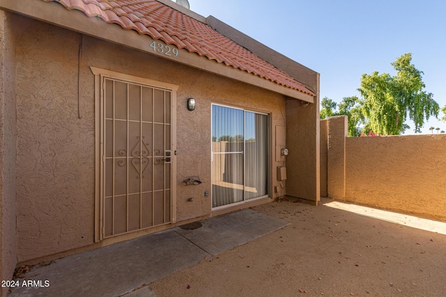 entrance to property featuring a tile roof, a patio, fence, and stucco siding