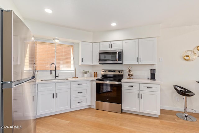 kitchen with light wood-style flooring, stainless steel appliances, a sink, white cabinets, and light countertops