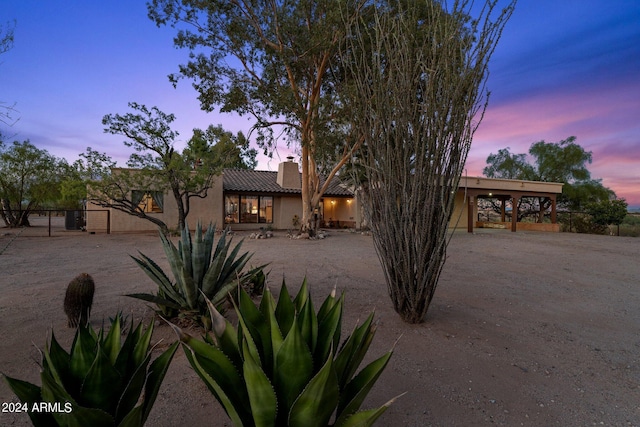 southwest-style home featuring fence, a tile roof, dirt driveway, stucco siding, and a chimney