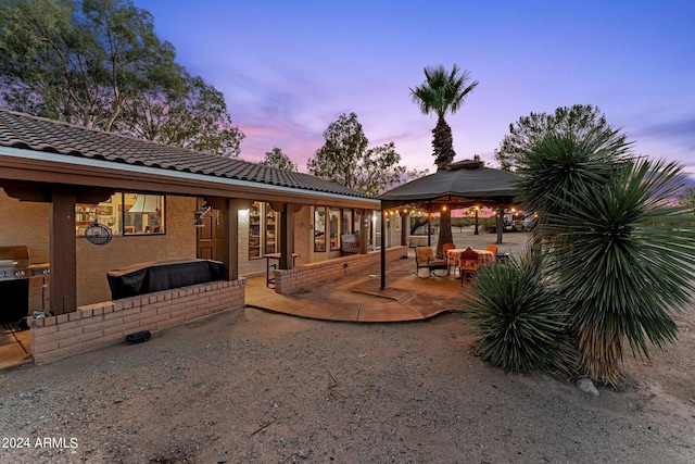 back of house at dusk featuring a gazebo, a tile roof, a patio, and stucco siding