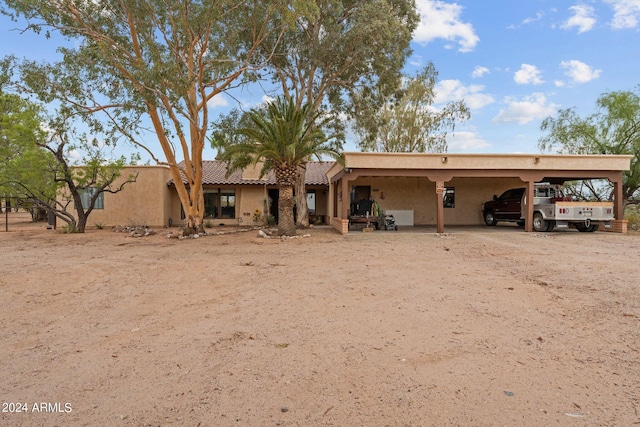 rear view of house featuring dirt driveway, a carport, and stucco siding