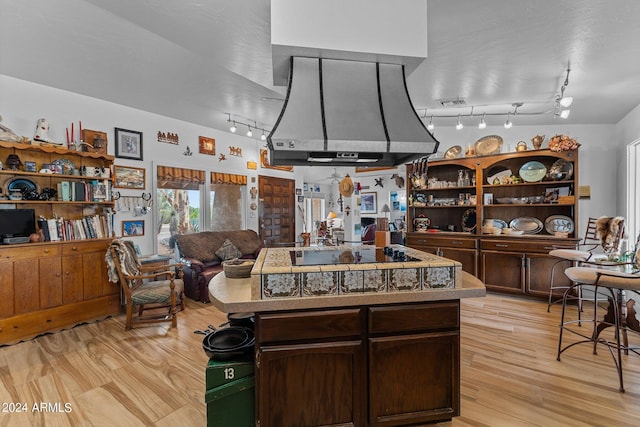 kitchen featuring dark brown cabinetry, open floor plan, range hood, black electric cooktop, and light wood-type flooring