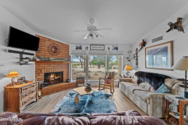 living area with visible vents, a ceiling fan, wood finished floors, vaulted ceiling, and a fireplace