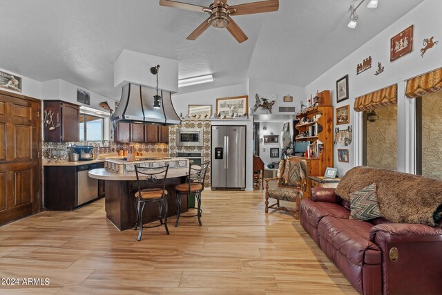 kitchen featuring lofted ceiling, stainless steel appliances, island range hood, backsplash, and dark brown cabinetry