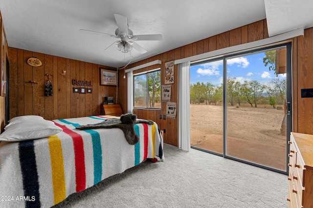 bedroom featuring access to exterior, light colored carpet, ceiling fan, and wooden walls