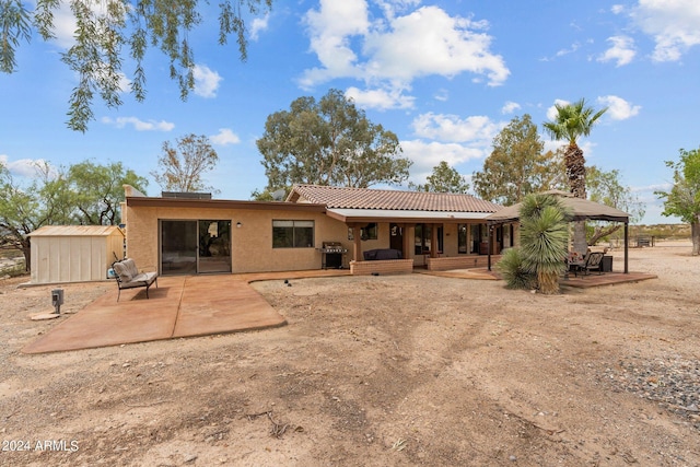 back of house with an outbuilding, a patio, a tile roof, stucco siding, and a shed