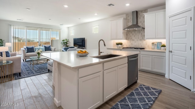 kitchen with a center island with sink, white cabinetry, light wood-type flooring, wall chimney exhaust hood, and sink