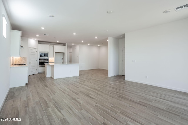 unfurnished living room featuring sink and light hardwood / wood-style flooring