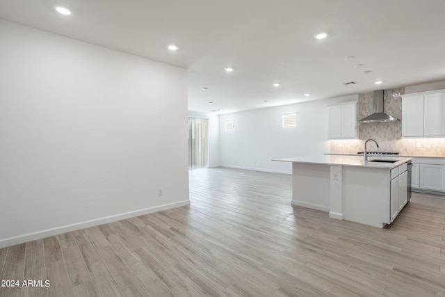 kitchen featuring white cabinets, a kitchen island with sink, light wood-type flooring, wall chimney exhaust hood, and sink