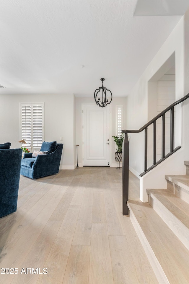 entryway featuring a notable chandelier, visible vents, baseboards, light wood-style floors, and stairway