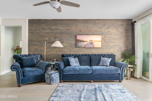 living area featuring ceiling fan, an accent wall, wood finished floors, and wooden walls