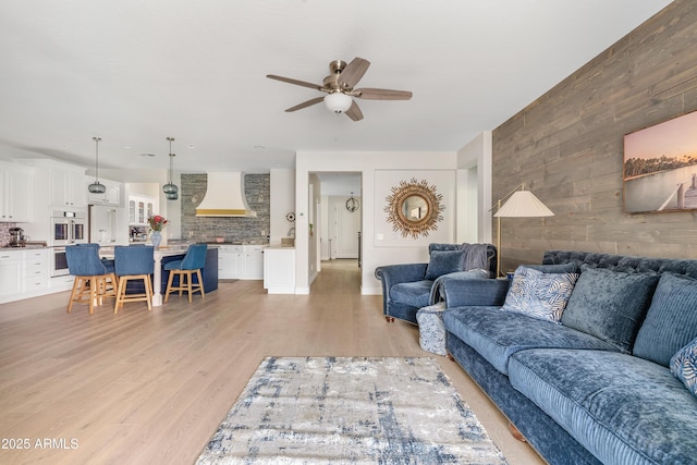 living room featuring light wood-style floors, an accent wall, wood walls, and a ceiling fan