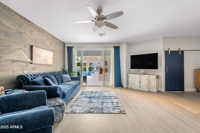 living area with visible vents, ceiling fan, wooden walls, and wood finished floors