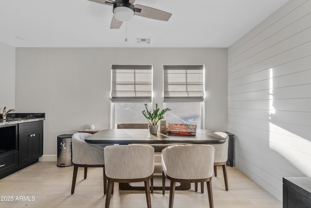 dining area with light wood-style flooring, visible vents, ceiling fan, and wooden walls