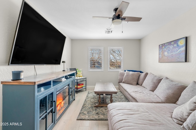 living room featuring light wood finished floors, ceiling fan, visible vents, and baseboards