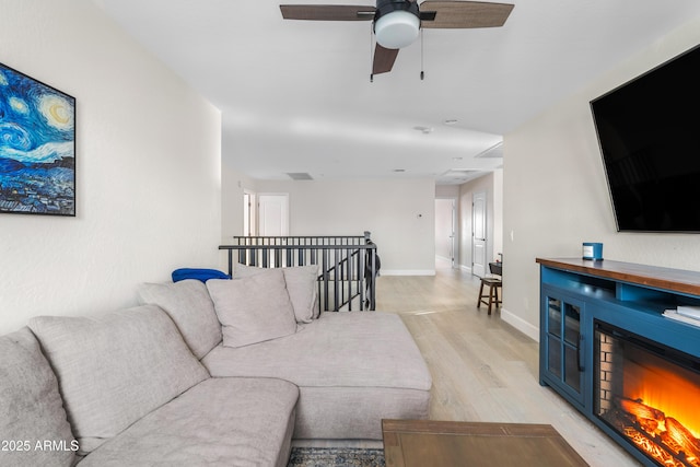 living room featuring light wood-style floors, baseboards, a ceiling fan, and a glass covered fireplace