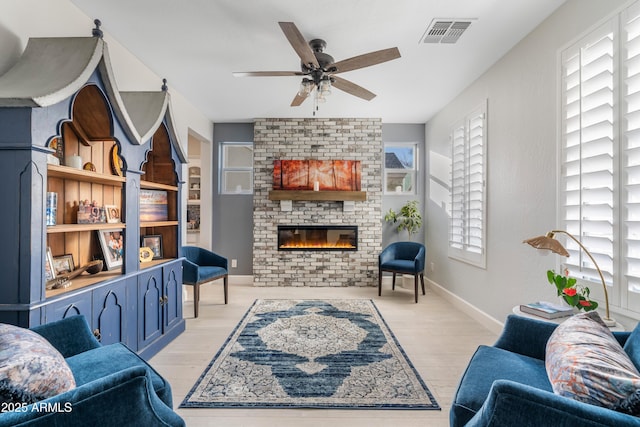 living area with baseboards, visible vents, a ceiling fan, light wood-type flooring, and a brick fireplace