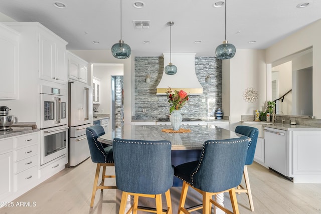 kitchen with visible vents, light wood-style flooring, white cabinets, white appliances, and a kitchen bar