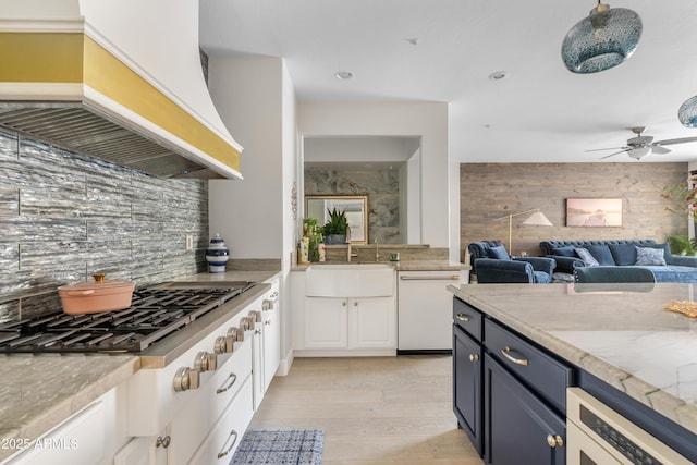 kitchen featuring custom exhaust hood, backsplash, white cabinetry, a sink, and dishwasher