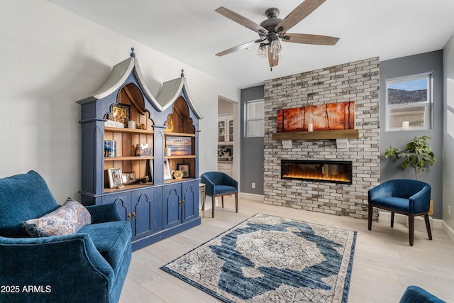 living area with a brick fireplace, wood finished floors, a ceiling fan, and baseboards