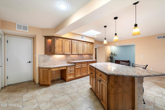 kitchen with brown cabinets, backsplash, visible vents, and a kitchen breakfast bar