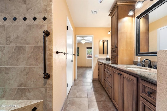 bathroom with ceiling fan, tiled shower, visible vents, a sink, and double vanity