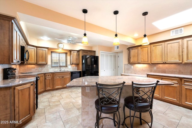 kitchen featuring tasteful backsplash, light stone counters, a center island, black appliances, and a sink