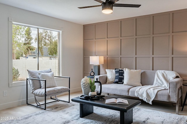 living room with a decorative wall, ceiling fan, and light wood-style floors