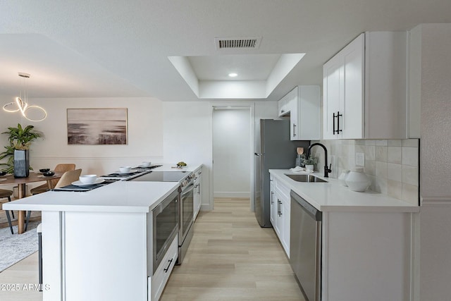 kitchen with visible vents, a sink, stainless steel appliances, light countertops, and a raised ceiling