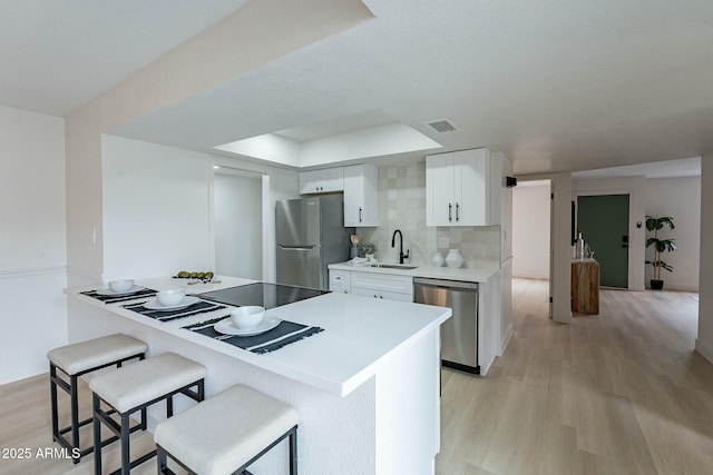 kitchen featuring light wood finished floors, a breakfast bar, stainless steel appliances, decorative backsplash, and white cabinets