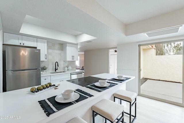 kitchen with a kitchen bar, a sink, white cabinetry, stainless steel appliances, and light countertops