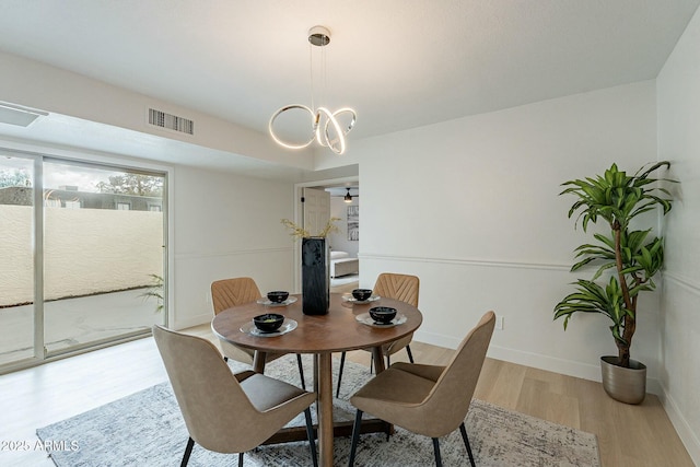 dining room with a notable chandelier, visible vents, baseboards, and wood finished floors