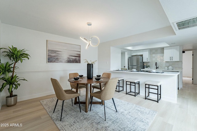 dining area with visible vents, baseboards, light wood-style floors, and a chandelier