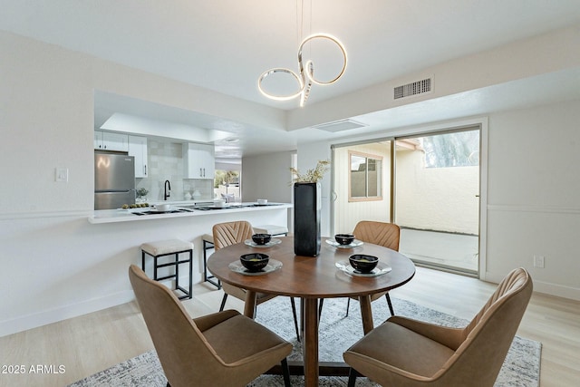 dining space with light wood-type flooring, visible vents, a raised ceiling, an inviting chandelier, and baseboards