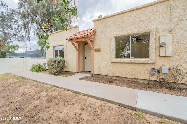 view of front of property with stucco siding, fence, and a tile roof