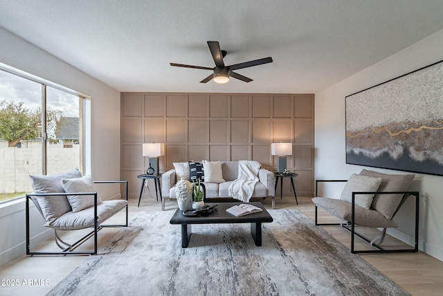 living room with light wood-type flooring, baseboards, a textured ceiling, and ceiling fan