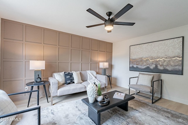 living area featuring baseboards, light wood-style floors, a ceiling fan, and a decorative wall