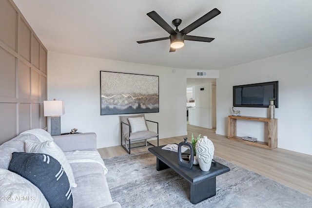 living room with baseboards, a ceiling fan, visible vents, and light wood-type flooring