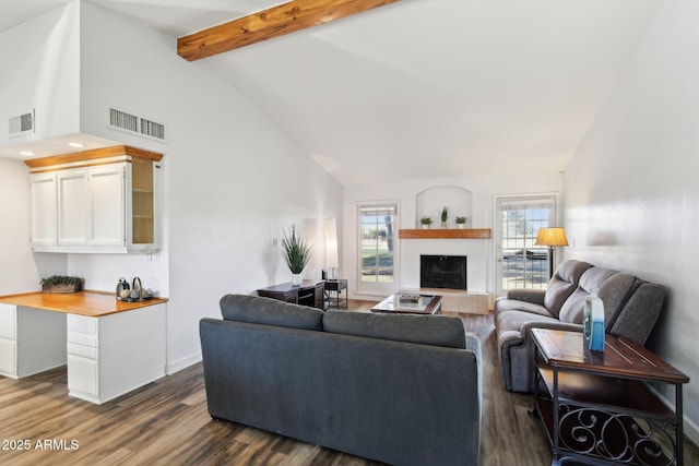 living area with beam ceiling, visible vents, a fireplace with raised hearth, and dark wood-style flooring