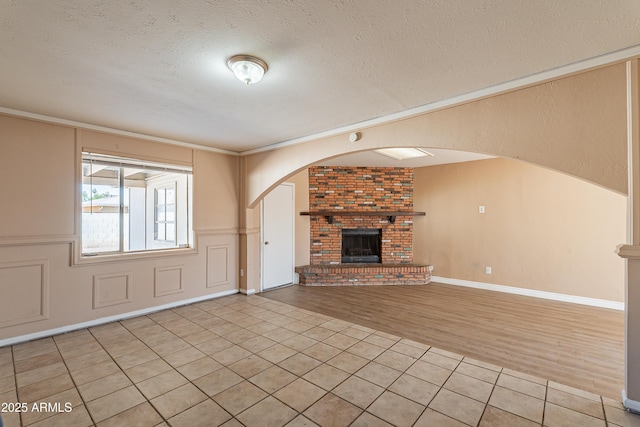 unfurnished living room with crown molding, light tile patterned flooring, a textured ceiling, and a fireplace