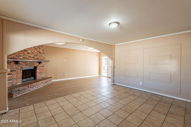 unfurnished living room with crown molding, a brick fireplace, light tile patterned floors, and a textured ceiling