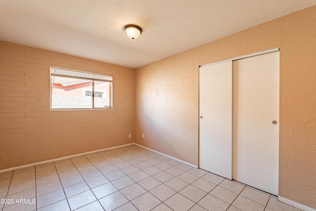 unfurnished bedroom featuring light tile patterned floors, a closet, a textured ceiling, and brick wall