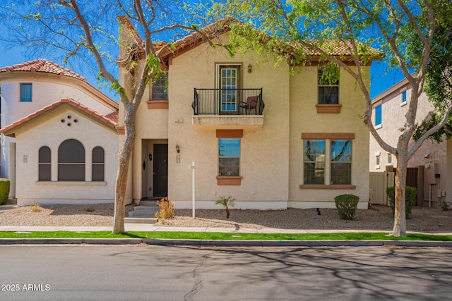 mediterranean / spanish-style home with a balcony, a tile roof, fence, and stucco siding