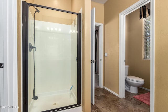 bathroom featuring a stall shower, toilet, and baseboards