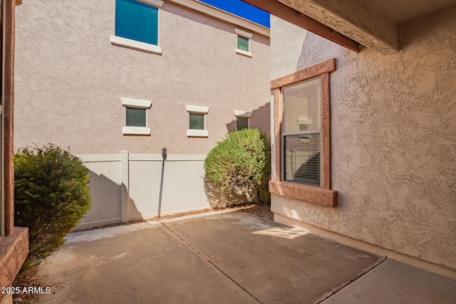 view of side of property with a patio area, fence, and stucco siding