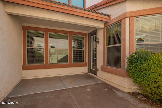 entrance to property featuring a patio area, a tiled roof, and stucco siding