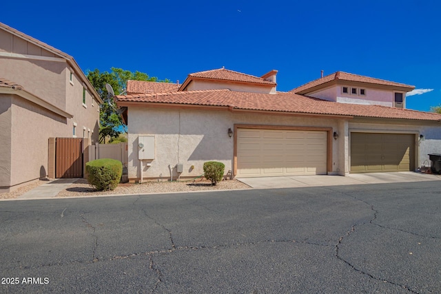 view of front of house with a tiled roof, an attached garage, a gate, fence, and stucco siding