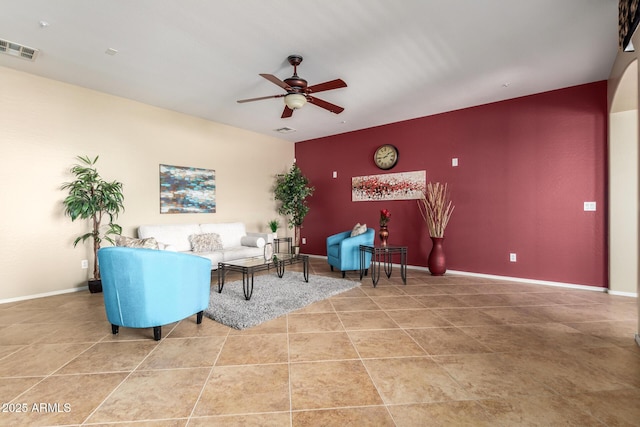 living area featuring light tile patterned floors, visible vents, baseboards, ceiling fan, and an accent wall